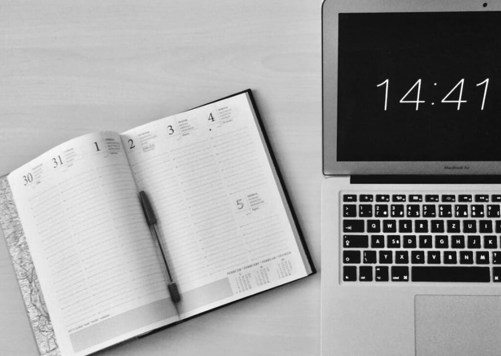 An open planner on a desk next to a laptop showing the time 14:41