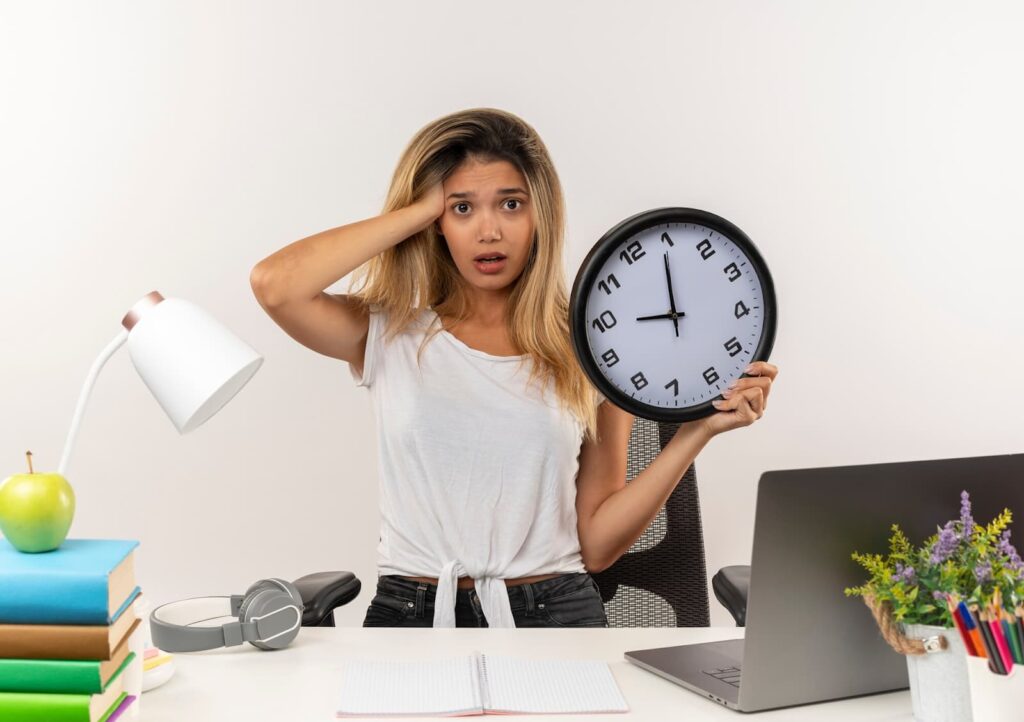 A girl sitting at a table and putting her hand on her head while holding a watch