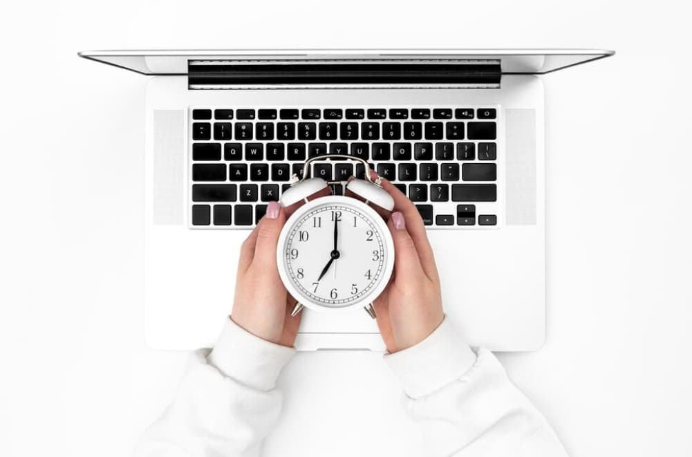 Hands holding a clock over a laptop keyboard