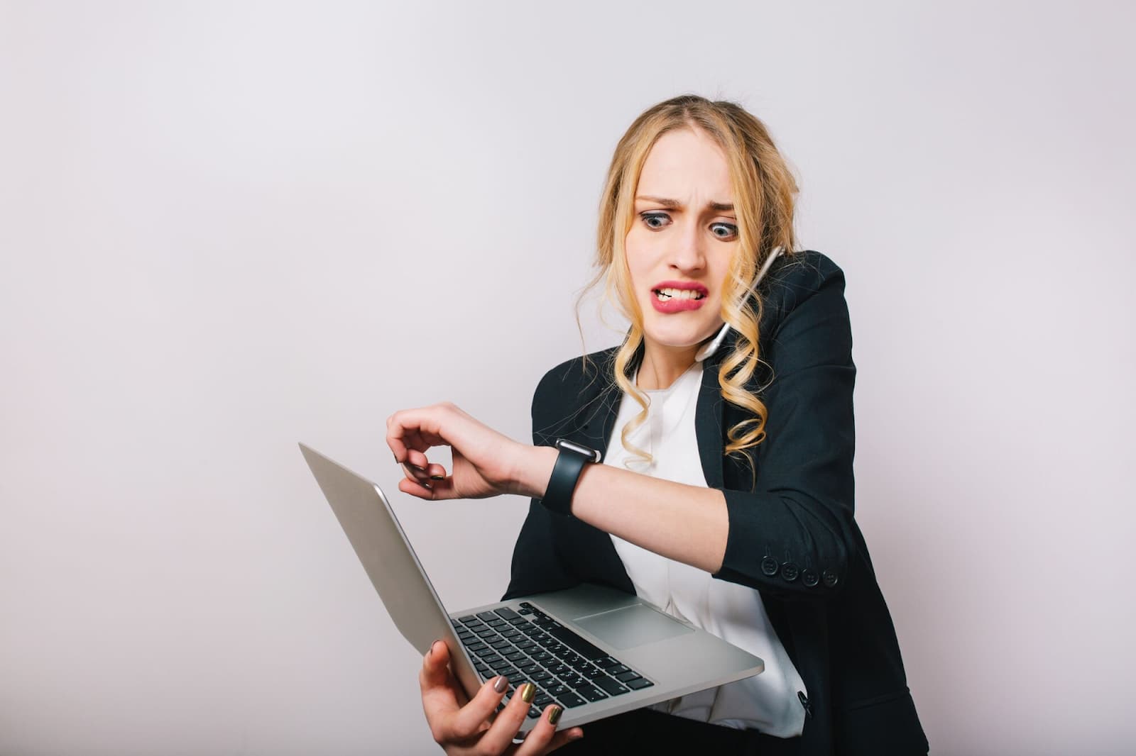 Business woman in a formal suit with a laptop, talking on the phone and looking at her watch