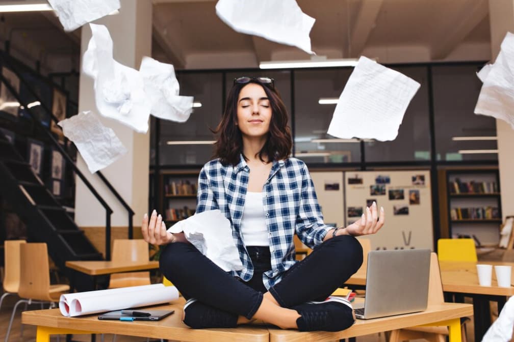 A woman meditates amid flying papers in an office