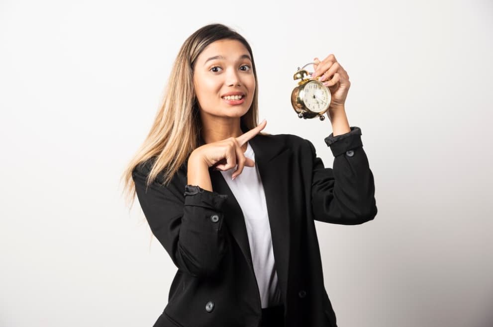 A smiling woman in a suit pointing to a small vintage alarm clock