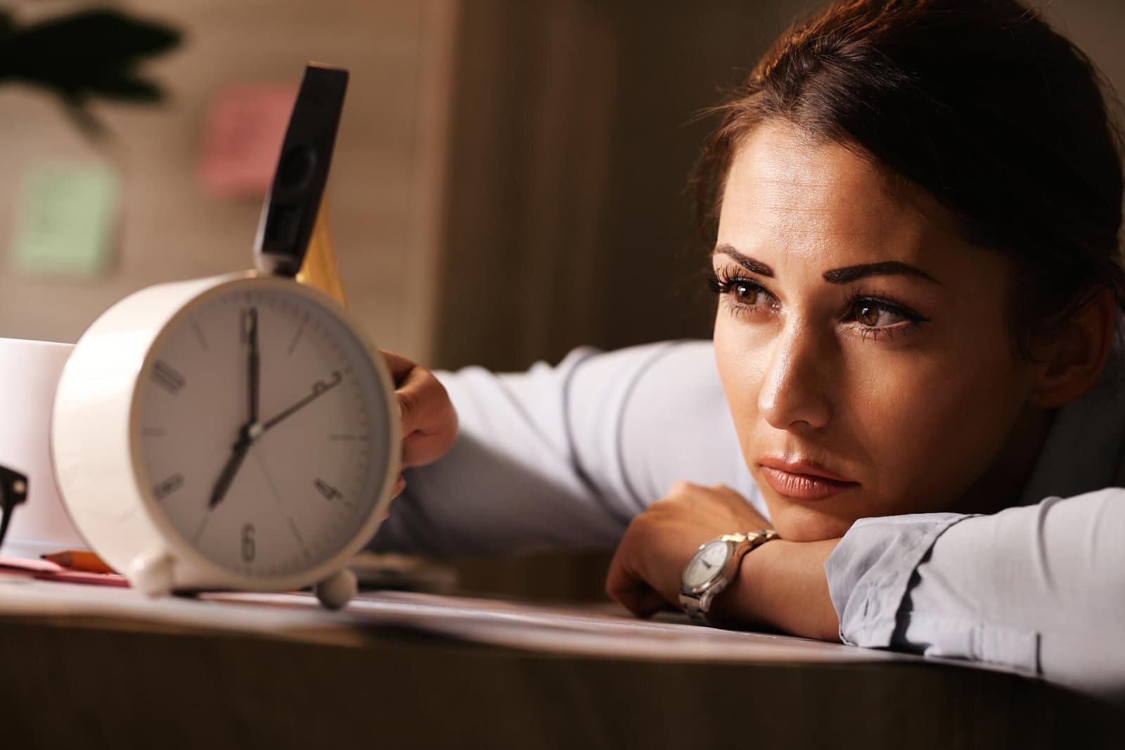 Displeased business woman hitting alarm clock with hammer in the office