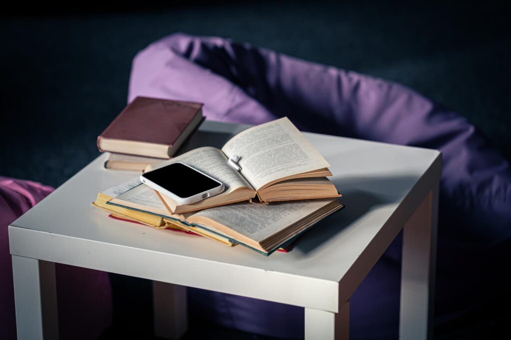 Books on a small white table on a blurred background of the interior with poufs