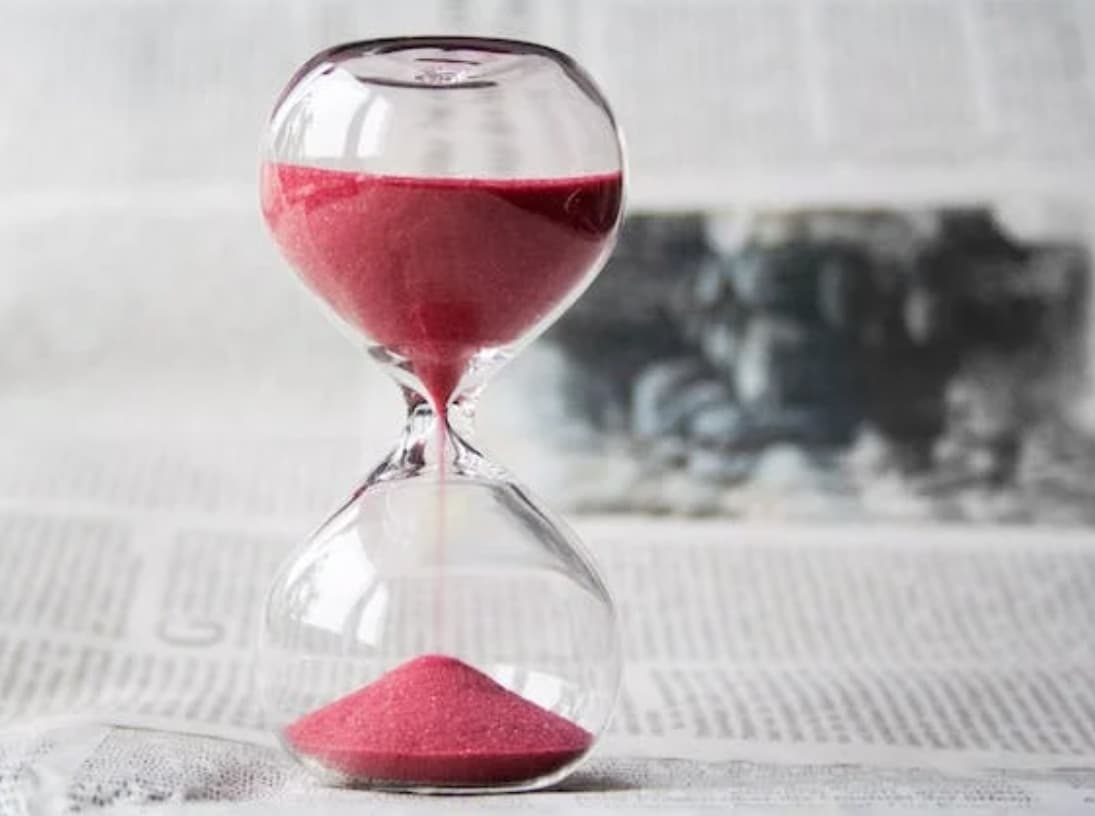 An hourglass with pink sand on a newspaper background