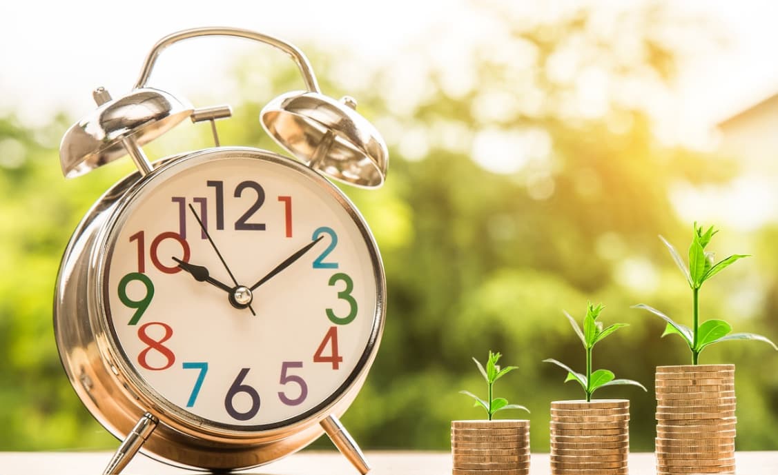 Alarm clock and growing coin stacks representing financial growth over time