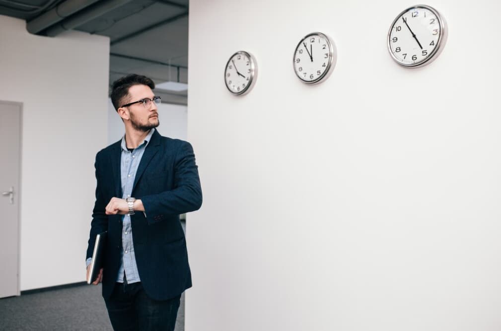 Man in a suit checking his watch near three wall clocks