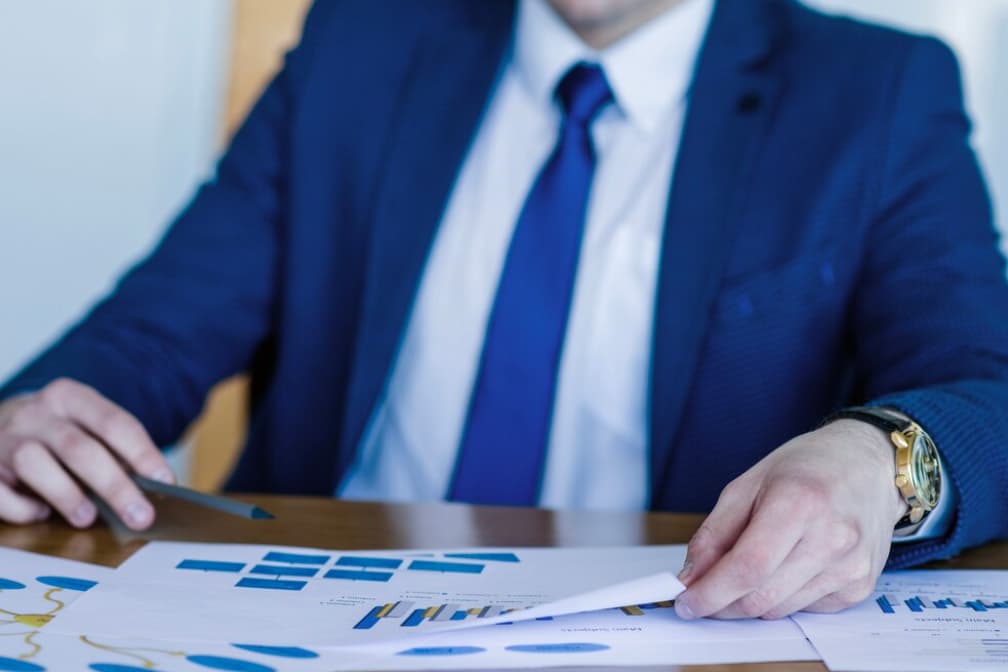 man in classic suit sitting in the office and holds hands on the table with sheets on it